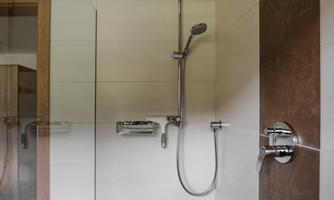 A modern shower with smooth tiles and a large rainwater showerhead. The decor is simple and stylish, with an elegant color contrast.