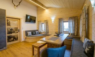 A cozy living space with wooden paneling, a large table, and comfortable seating. Large windows let in plenty of light and create a pleasant atmosphere.