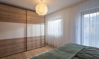 A modern bedroom with a large wooden wardrobe and a cozy bed. Soft curtains let gentle light in.