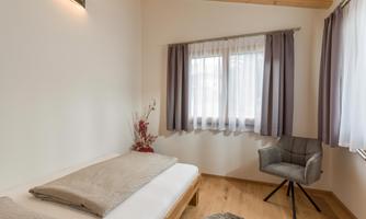 A modern bedroom with a single bed and soft colors. Large windows provide plenty of daylight and a cozy atmosphere.