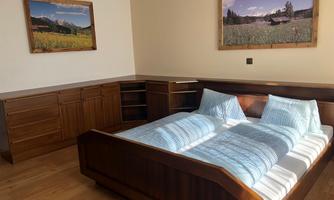 A cozy bedroom with a wooden bed and blue blankets. Pictures of landscapes hang on the walls.