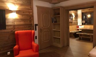 A cozy room with wood-paneled walls and warm light. A striking red armchair stands next to an open door, which leads to another area.