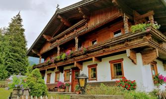 A traditional wooden house in alpine style with beautiful flower boxes and an inviting porch. Surrounded by lush greenery and trees.