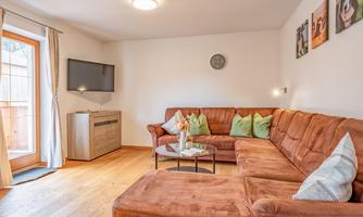 An inviting living room with a comfortable brown couch and a glass table. Large windows provide plenty of daylight and a cozy atmosphere.