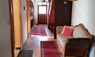 An inviting hallway with wooden floors and red carpets. On the left, there is a cozy couch, and the stairs lead upstairs.