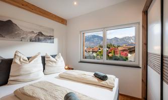 A modern bedroom with two beds and large windows. Outside, a beautiful mountain landscape can be seen.