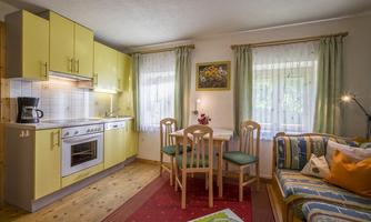 A bright kitchen with yellow cabinets and a small dining area. A cozy sofa with cushions complements the room.