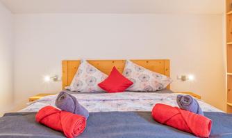 A cozy bedroom with a large bed and colorful towels. The walls are bright and the decoration is simple and inviting.