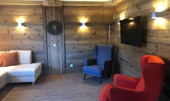 A cozy room with wooden walls and modern light sources. Two armchairs, one in blue and one in red, as well as a sofa in white create an inviting atmosphere.