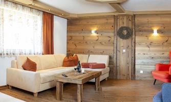 A cozy living space with wooden paneling and a bright color scheme. The decor includes a beige couch and stylish chairs in red and blue.