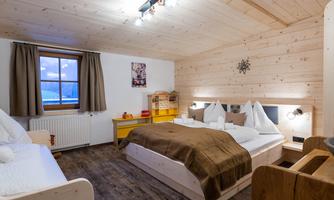 A cozy bedroom with wooden walls and modern furniture. There are two beds, a window with curtains, and a friendly designed atmosphere.
