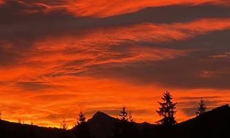 A breathtaking sunset with a vividly orange sky. Silhouettes of trees and mountains are visible in the foreground.