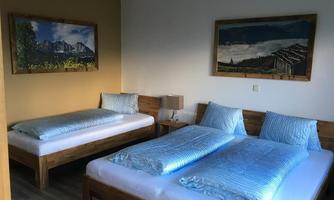 A cozy room with two single beds and light blue bed linens. Pictures of mountains and landscapes hang on the walls.