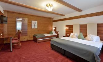 A cozy hotel room with two beds, a table, and a chair. The walls are made of wood and the floor is carpeted.