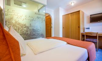 A cozy room with a double bed and orange bedding. The room features a desk and a television.