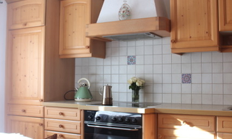 A modern kitchen with wooden furniture and a stove. On the countertop, there is a coffee pot and a flower vase.