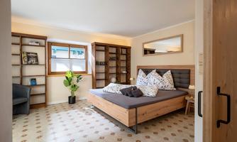 A cozy bedroom with a large bed and beautiful pillows. Shelves with books and a plant create an inviting atmosphere.