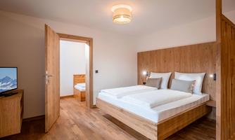 A modern bedroom with a double bed. The room is bright and friendly, with a television and access to another sleeping area with a single bed.