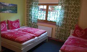 A cozy bedroom with two beds and colorful bedspreads. Large windows let in plenty of daylight and provide a view of nature.
