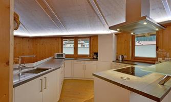 A modern kitchen with wooden paneling and large windows. The equipment includes a stove, a sink, and various kitchen appliances.