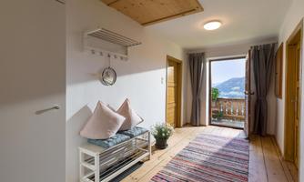 A bright hallway with a wooden floor and a cozy seating area. The open door provides a beautiful view of the mountains.