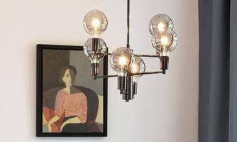 A modern ceiling lamp with several light bulbs hangs above a painting of a woman. In the background, gray curtains can be seen.