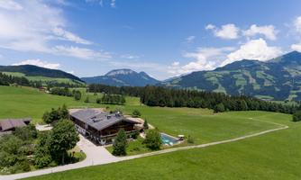 An impressive landscape with a large meadow, mountains in the background, and a beautiful building. The scene shows a clear sky and tranquil nature.