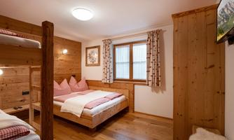A cozy bedroom with wooden furniture and a large window. There is a double bed and a bunk bed suitable for children.