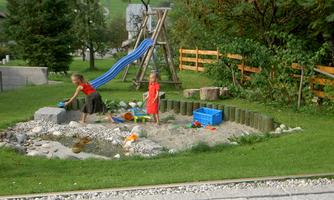 A playground with a slide and a sandpit. Two children are playing and exploring nature.
