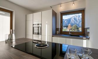 A modern kitchen with glossy white cabinets and a wooden table. Through the window, you can see a picturesque mountain landscape.