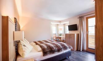 A bright and cozy bedroom with a large bed and a television. Large windows offer a view of a balcony.