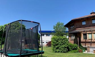 A garden with a trampoline and a beautiful wooden house. The sky is clear and blue, it is a sunny day.