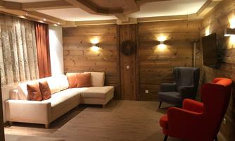 A cozy living space with wood paneling and warm lighting. Two comfortable armchairs in red and blue complement the bright couch with cushions.