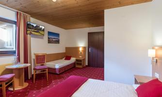 A bright hotel room with two beds and a comfortable chair. Pictures hang on the walls, and the room features a warm, inviting wooden floor.