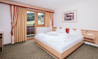 A cozy bedroom with a large bed and white bedcovers. Through the window, the green landscape is visible.