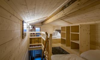 A cozy attic room with wooden paneling and bright shelves. A ladder leads up to a sleeping area.