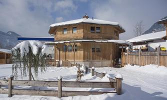 A wooden house in the snow, surrounded by a snow-covered landscape. The sky is partly cloudy and the atmosphere is calm and wintry.