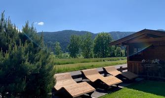 A quiet garden with loungers and a wooden house. In the background, green trees and gentle hills are visible.