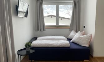A modern room with two beds and a small table. The window offers a view of a mountain landscape.