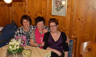A cheerful gathering of three people at a beautifully set table. In the background, there are wooden paneling and a floral painting visible.