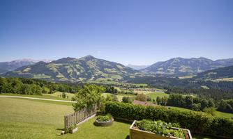A picturesque landscape with gentle hills and extensive mountains in the background. The sky is clear and blue, perfect for a beautiful day in nature.