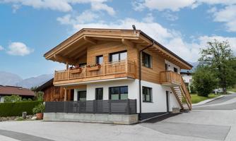 A modern wooden house with balconies and large windows. It is situated in a quiet location with a beautiful sky in the background.
