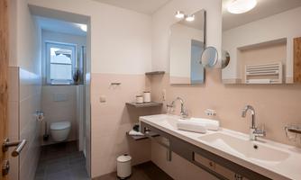 Modern bathroom with double sink, large mirror, shower, toilet, and towel warmer.