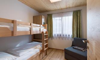A simple bedroom with a bunk bed and a small sofa.  
Bright walls and a large window create a friendly atmosphere.