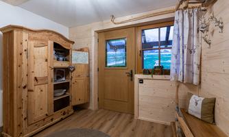 A cozy room with wooden paneling and a rustic wardrobe. The entrance door has a window that shows a beautiful view.