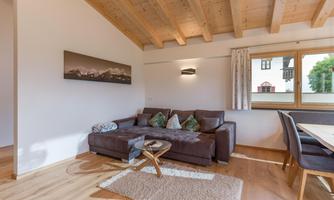 A modern living room with a brown sofa and an elegant table. The high wooden ceilings and the large window create a bright, inviting atmosphere.