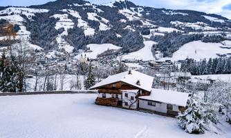 A snowy landscape with a spacious little house and mountains in the background. The scene conveys a calm winter atmosphere.