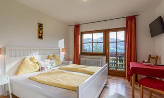 A cozy bedroom with two single beds and yellow pillows. The windows offer a view of the mountain landscape.