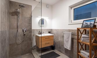 A modern bathroom with a walk-in shower and a stylish sink. Wooden shelves hold towels and decorative elements.