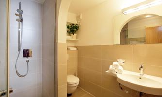 A modern bathroom with a shower and a sink. The walls are bright and there is a small plant on the shelf.